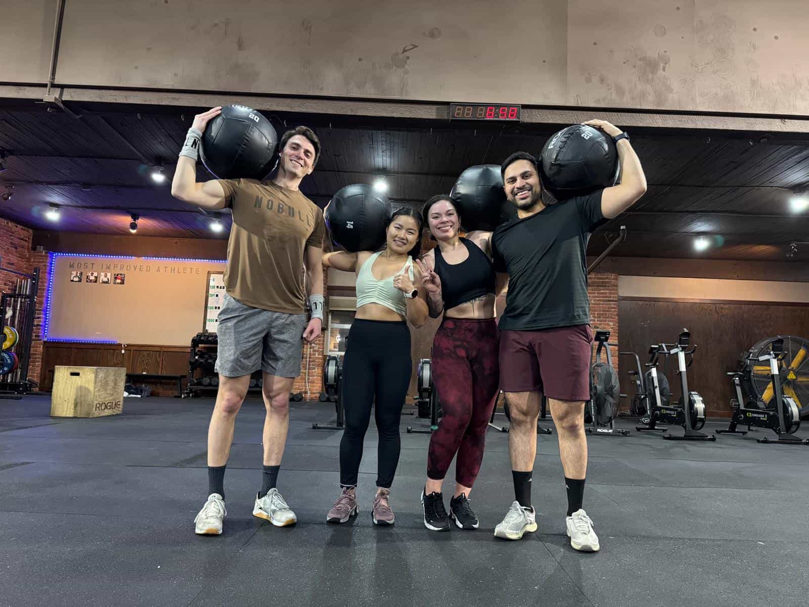 Four Persistence Athletics members holding wall balls in front of the Most Improved Athlete wall, Belltown Seattle