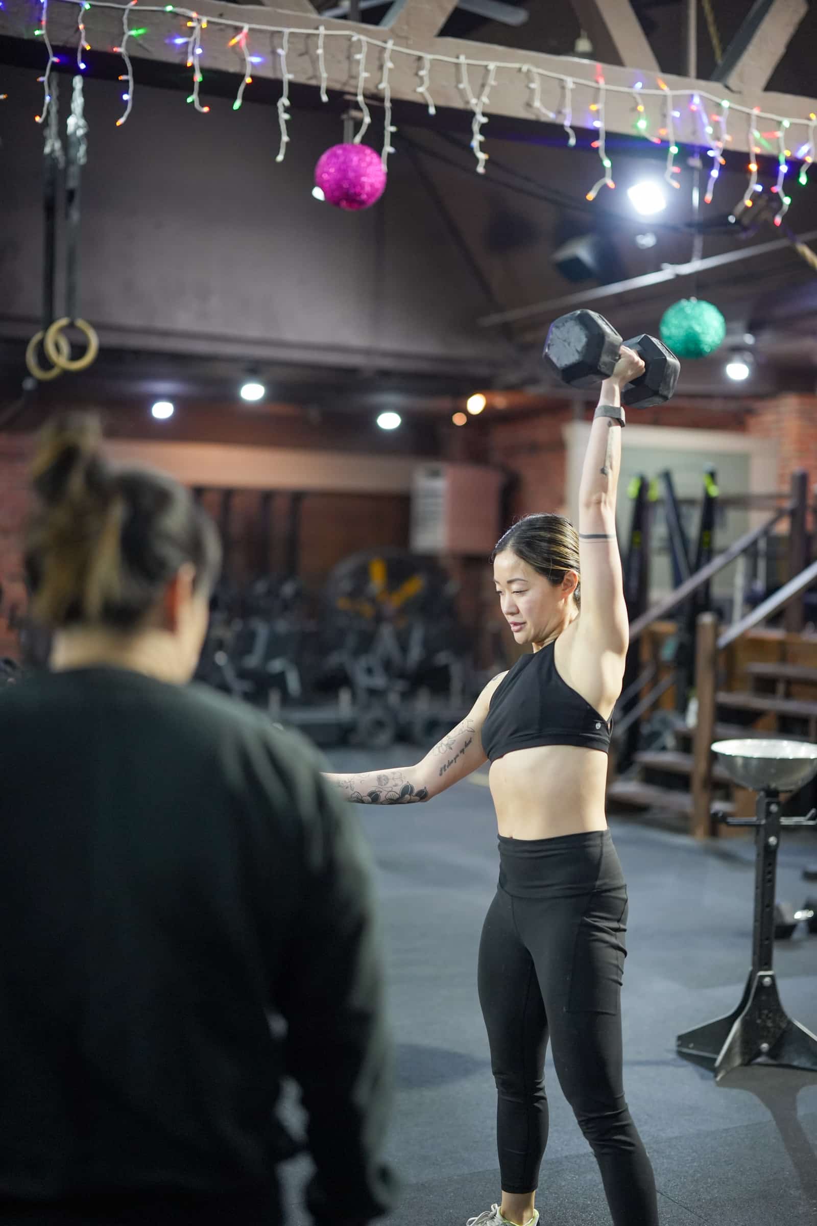 Coach watching a member press an overhead dumbbell rep at Persistence Athletics, Belltown Seattle